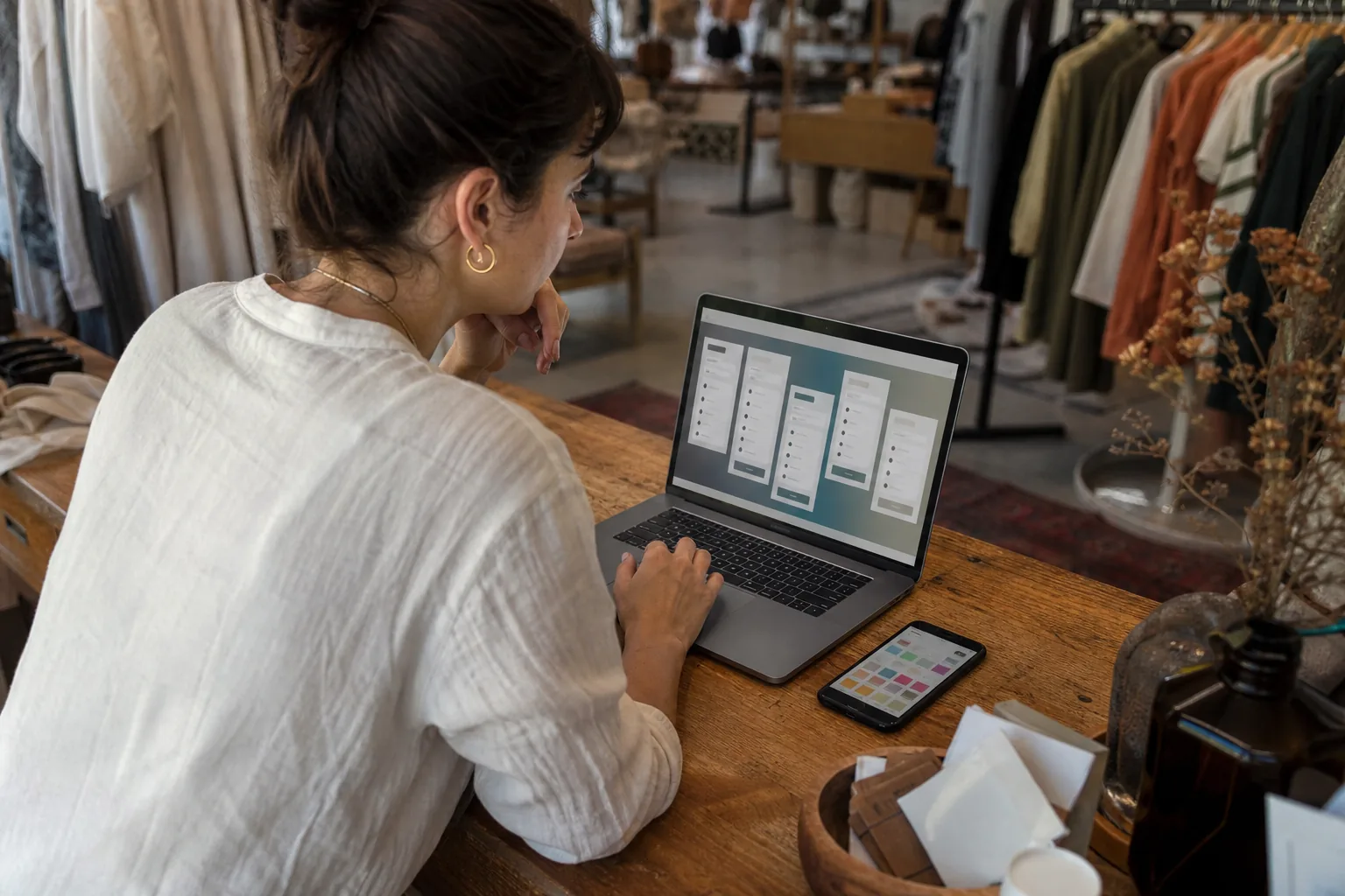 Boutique owner comparing social media scheduler plans on a laptop with a phone showing a calendar grid